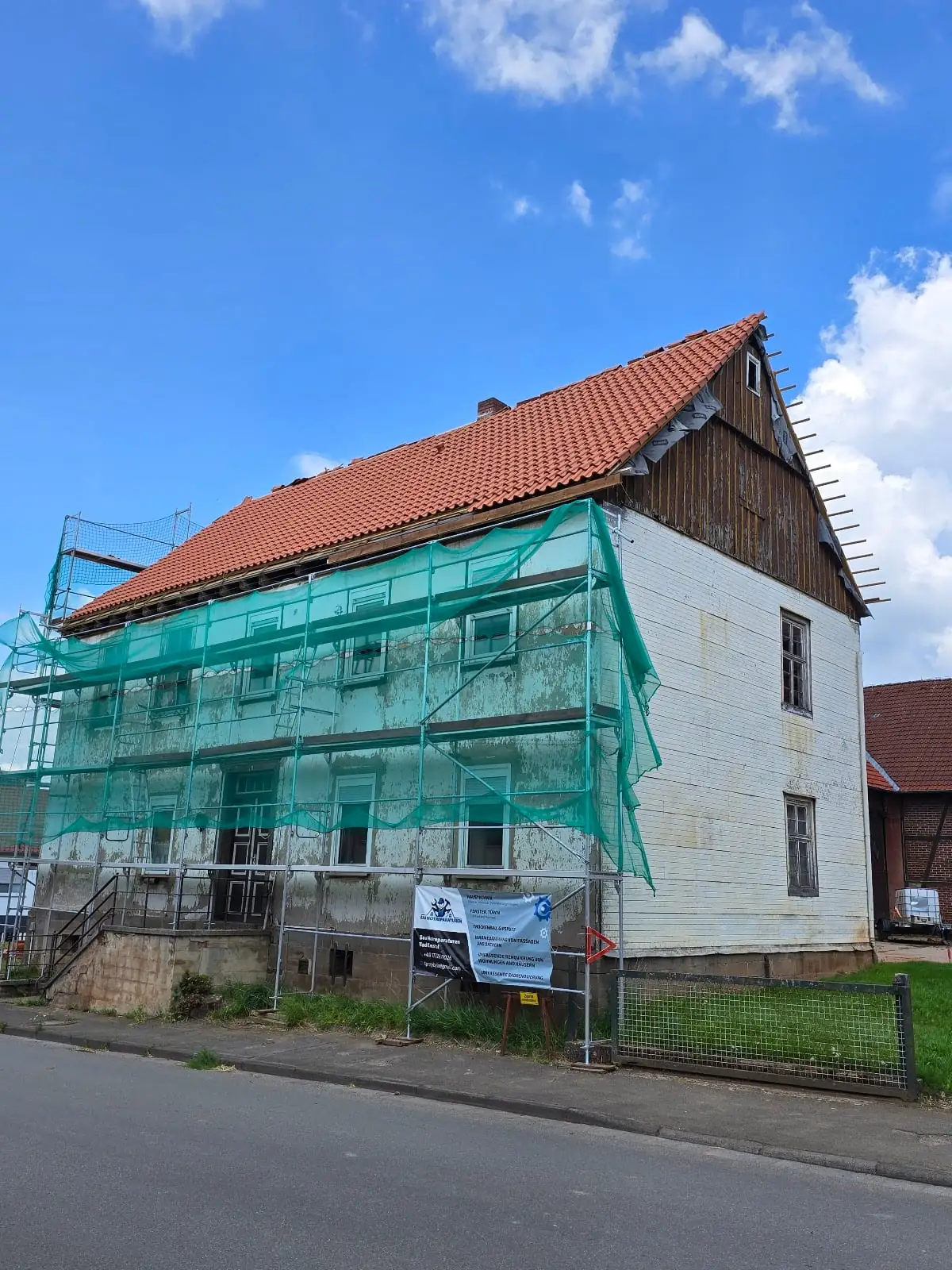 Altbau im Gerüst mit dem Banner des Betriebs an der Fassade