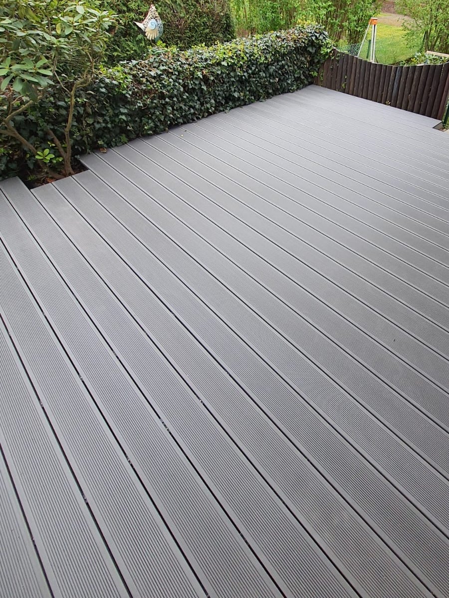 Fertig verlegte Terrasse aus grauen Dielen an einem Holzhaus